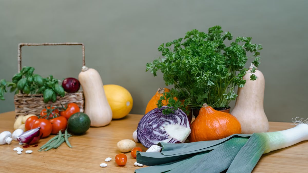A diverse assortment of fresh vegetables including squash, tomatoes, and greens on a wooden table.