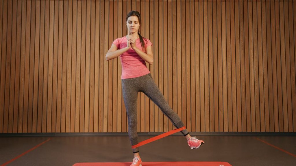 A woman performs leg exercises with a resistance band at a gym, promoting fitness and healthy living.