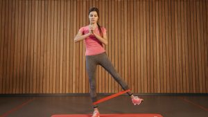 A woman performs leg exercises with a resistance band at a gym, promoting fitness and healthy living.